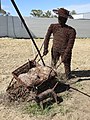 Artwork made from barbwire, of a person pushing a wheelbarrow, with a dog (2021).