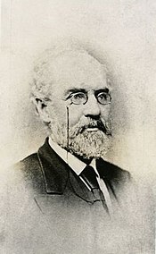 Black and white photograph of a bearded man wearing eyeglasses, a suit, and tie.