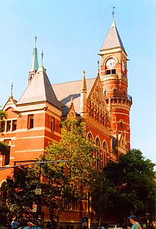 A red brick building with extensive ornamentation and large clock faces in a tower.