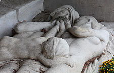 In a section of the tomb an angel shines a light over a dead couple across whose chests lies a dead child.