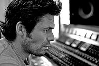 A sepia picture of a man posing in front of a mixing board.