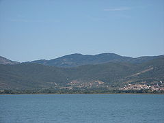 A colour photograph from the middle of a lake of the lake shore with low hills beyond