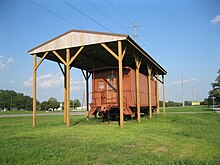 Photo shows a caboose under a wooden cover on an old railroad right-of-way