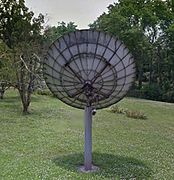 The back side of an old C-band satellite dish showing the pole, mount, motor, and structure of the dish.