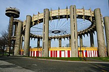 The New York State Pavilion as seen from the southwest. At center-right is the Tent of Tomorrow, an elliptical structure with concrete columns surrounding a set of girders. To the left are three abandoned observation towers.