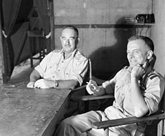 Two men in light-coloured uniforms seated at a table