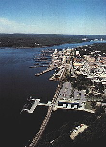 An aerial view of a naval base next to a wide river. A rail line runs through the base near the river bank.