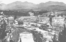 Birger Ruud pendant un saut, avec la zone d'arrivée et les montagnes en arrière-plan
