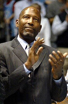 A man wearing a gray suit looking up while clapping.