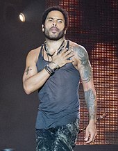 Lenny Kravitz onstage in a tank top, while placing his right hand on his chest