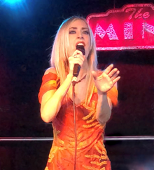 Maria Entraigues-Abramson in an orange dress singing into a microphone