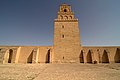 Gros plan sur la façade nord de l'édifice. Au milieu du mur, pourvu de contreforts à toit en pente, se dresse l'imposant minaret crénelé.