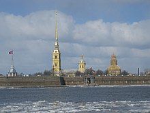 Photographie couleurs de quatre flèches de monuments dépassant d'un mur de forteresse devant un fleuve.