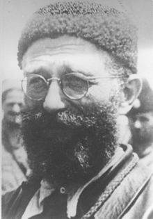 Un homme d'une quarantaine d'années, portant des lunettes, barbu et coiffé d'une toque de fourrure.