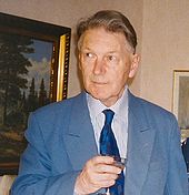 Colour photograph of Paul Britten Austin holding a wineglass in front of an oil painting