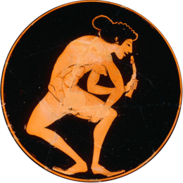 The inside of a wide black cup. In a red circle is the figure of a standing woman holding two phalluses; one she is about to place in her vagina, one she is about to place in her mouth