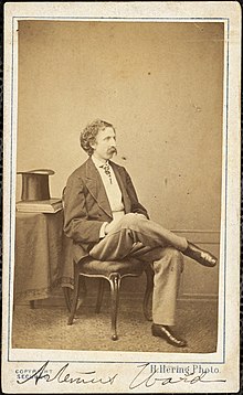 Photograph of Artemus Ward, sitting with his right leg crossed over his left, a top hat and books sitting on the table to his right. A typed caption at the bottom of the image reads "H. Hering Photo" and his name is written at the bottom.
