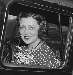 A smiling white woman with dark hair and wearing a polka-dot dress, sitting in an airplane cockpit