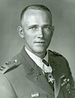 Head and shoulders of a white man with short hair, wearing a military jacket with a star-shaped medal hanging from a ribbon around his neck.