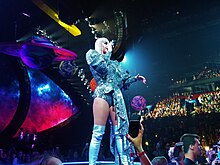 An image of Perry performing in front of an audience, wearing a metallic outfit with thigh-high boots.