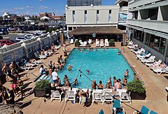 Photo of a swimming pool on a sunny day, with many people in and around the water