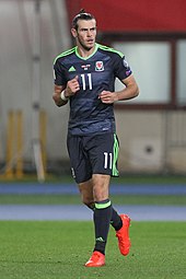 A football player wearing a dark football kit with neon trim.