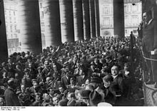 Photo en noir et blanc montrant une foule d'hommes serrés sous un porche à haute colonnes