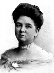 A light-skinned woman with dark hair in a bouffant updo