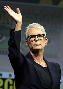 Photo d'une femme avec des lunettes qui lève la main.