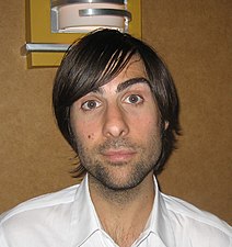 Photographie en buste d'un jeune homme aux cheveux bruns portant une chemise blanche.