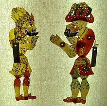 Two two-dimensional puppets against a lit screen. The puppets are in profile view facing each other, and they each have segmented limbs.