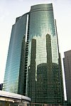 Ground-level view of a high-rise's green, curved, reflective glass facade; it is bisected by a vertical groove