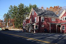 A road intersection with a stone monument in the background and a red building in the foreground.