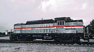 A gray diesel switcher locomotive with black roof and underside. On the side are red, white, and blue stripes of equal width.