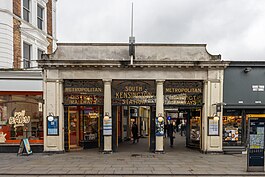 Station entrance with portico and ornamental ironwork signage above stating "Metropolitan and District Railways", "South Kensington station".
