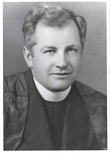 Black and white photo of man wearing a black robe and white priest's collar