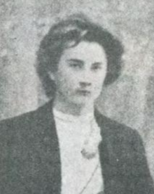 A young white man with longish tousled hair, wearing a dark jacket and a white shirt