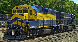 A blue and gold diesel locomotive with "2174" on it in several locations and "Middletown & New Jersey" on the side sits on a railroad track, seen from its front left. On its right, facing the opposite direction, is a mostly blue locomotive of a different model with "East Penn Railways" written on it in gold