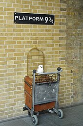 A sign reading "Platform 9+3⁄4" with half of a luggage trolley installed beneath, at the interior of King's Cross railway station.