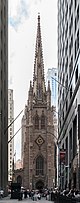 Ground-level view of a large, brown church with Gothic architecture and a tall, tapering spire that is only partially visible in the image