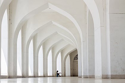 Corredor da Mesquita Nacional Baitul Mukarram, Daca, Bangladesh. A mesquita foi concluída em 1968 e tem capacidade para mais de 42 000 pessoas. O plano incluía lojas, escritórios, bibliotecas e áreas de estacionamento dentro do complexo. Embora haja uma tradição de mesquita de cúpula para muçulmanos, este edifício não manteve a regra da mesquita tradicional naquele tempo. Uma mesquita sem cúpula sobre o telhado de sua principal sala de orações foi uma experiência única. O templo foi construído quando o país fazia parte da República Islâmica do Paquistão. (definição 3 938 × 2 625)