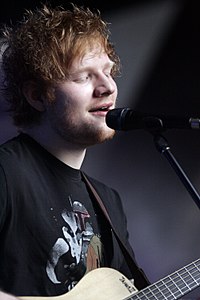 Ed Sheeran holding a guitar behind a microphone