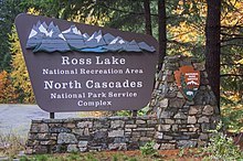 Outdoor sign with an image of mountain, the National Park Service logo, and the words "Ross Lake National Recreation Area, North Cascades National Park Service Complex"