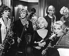 A ukulele-playing Monroe with a cross-dressing Lemmon in the bass and Curtis in the saxophone. There are also three other women playing different instruments.