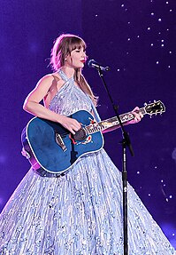 Taylor Swift wearing a midnight blue tinsel-fringed jacket singing on a mic