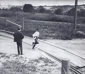 Un homme avec un béret passe sur un chemin de fer, un homme en costume le regarde.