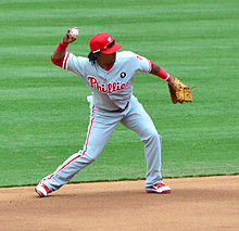 A young, dark-skinned man with dreadlocks throwing a baseball with his right hand