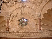 Photographie d'un oculus hexalobé à claustra, rempli de verres de couleur. Il orne l'espace compris entre les trompes cannelées, en coquille, de la coupole du mihrab.