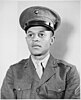 A monochrome photograph of a young male soldier with dark skin posing for an official portrait wearing the uniform of the United States Marine Corps