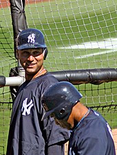 A man in a navy helmet and navy windbreaker smiles while talking to someone dressed in the same uniform who is turned away from the camera.